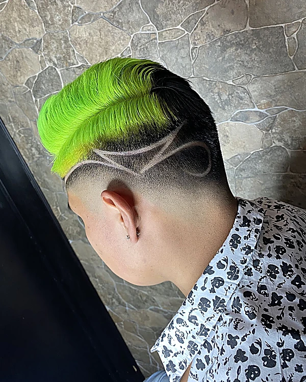 Cabello teñido verde neón peinado hacia un lado con un diseño rapado de líneas curvas y fade en la nuca