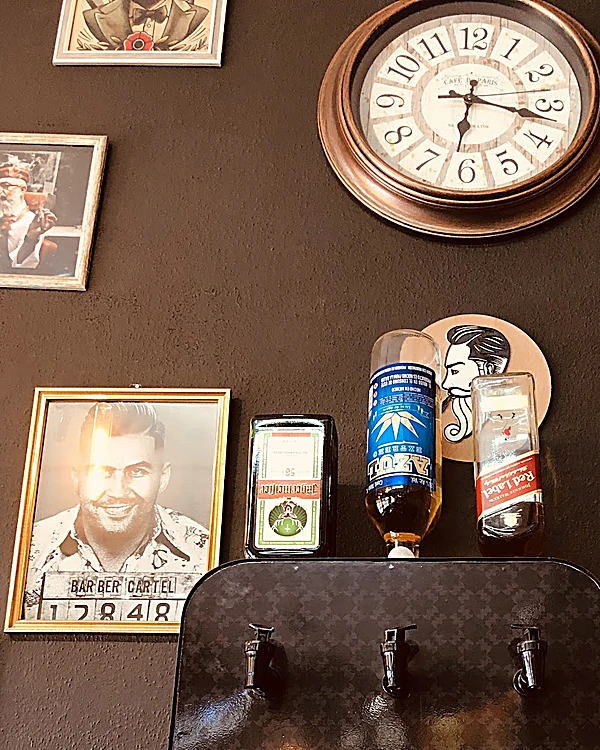 Reloj de cobre en el muro negro, un cuadro de un barbero con la placa Barber Cartel y un medallón con un barbero de bigote